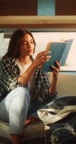 Vertical Screen: Young Adult Female Enjoying Her Time in a Motorhome, Relaxing and Reading an Adventure Book Story. Beautiful Girl Camping in a Caravan, Having a Journey to Rediscover Her True Self.