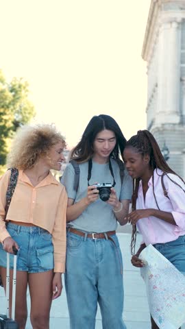 Three multiracial friends looking at the photos in a camera while sightseeing in Madrid, Spain.