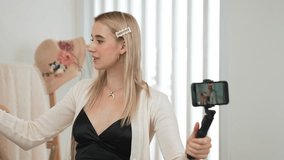 Young social medial content creator woman make fashion video using selfie stick. Blogger smile to camera while making persuasive online clothing sell vlog to audience or follower. Blithe