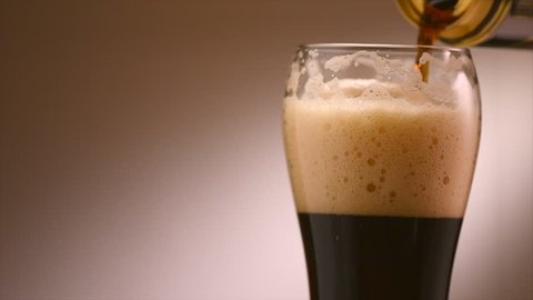 Pouring Cold Dark Beer into a glass. Can of Beer close up. Pint of beer rotated over brown background. Slow motion 4K video 3840x2160