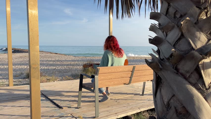 woman playing guitar sitting on a wooden bench in front of the sea