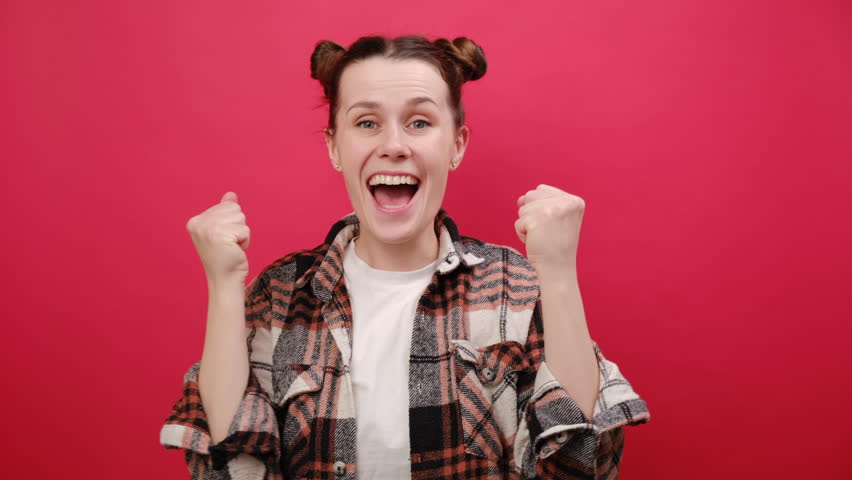 Portrait of excited pretty happy young woman 25 old years wearing casual clothes doing winner gesture celebrate clenching fist say yes, posing isolated over plain red color background wall in studio