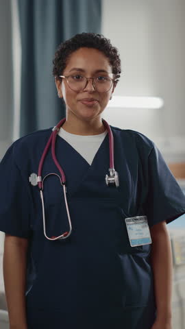 Vertical Screen. Hospital Ward: Portrait of Posing Beautiful Black Female Head Nurse, Doctor, Surgeon Smiles Charmingly and Kindly Looks at Camera. Modern Clinic with Advanced Equipment Royalty-Free Stock Footage #3444375915