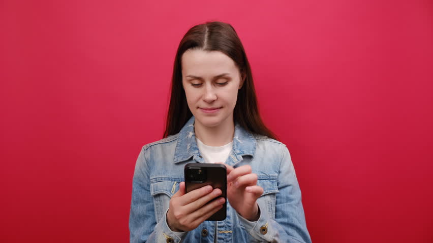Portrait of joyful young woman wear denim jacket use mobile cell phone typing say wow yes just found out great big win news doing winner gesture, posing isolated on red color background wall in studio