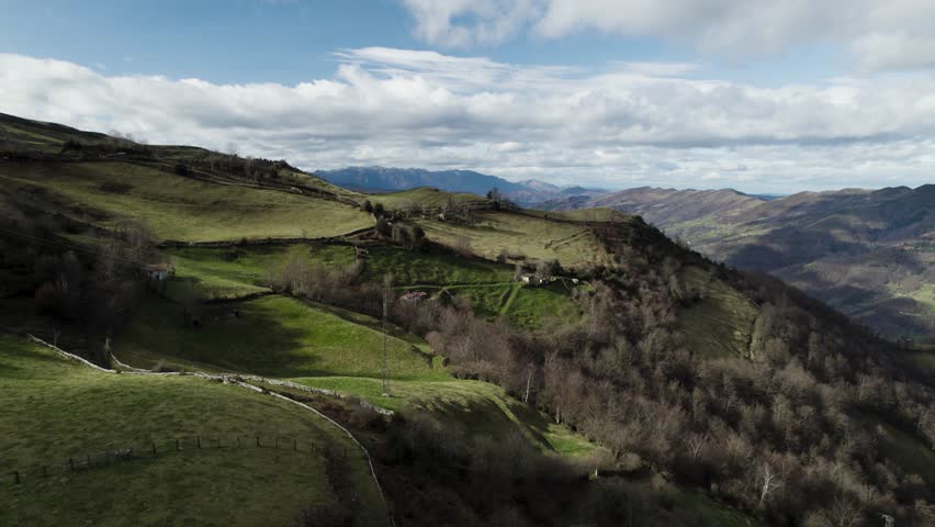 Flying over farmhouses built on high a grassy plateaus on top of a mountain range 