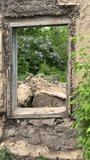 View of the lilac bushes through an old window in an abandoned house is like a natural painting in an old frame, vertical video.