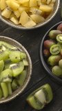 Three different types of kiwi fruit in bowls. Table spin. Vertical video.