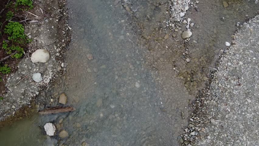 Aerial view of a car driving across the river stream in the middle of a gravel off road. 4x4 car is needed for the rocky terrain.