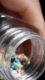 Vertical video. Sugar Balls in Rainbow Glaze Pour out of a Jar, Decorating Confectionery. Slow Motion on a Black Background.