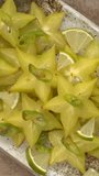 Top view of carambola or star fruit spicy salad with frozen green chili, lime pieces, and and lime juice. Perfect condiment for grilled fish or a curry. Table spin. Vertical video.