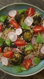 Roasted broccoli and quinoa salad with radish, tomatoes, and lamb's lettuce. Flat lay, table spin. Vertical video.