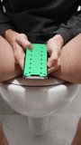 Vertical video. Barefoot Man Sitting on a Toilet Scrolls through a Green Screen with Tracking Marks, Layout. Slow Zoom In.