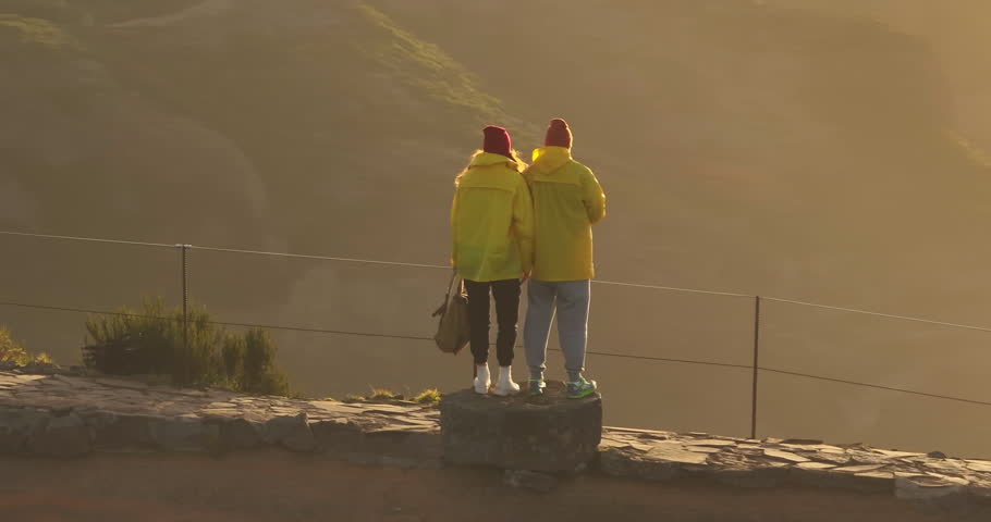 Two tourists teamwork with backpacks slow motion walking go silhouette in the sunlight glare of the sun at sunset. Camera follows couple on trip or adventure. Family walk in beautiful mountain valley
