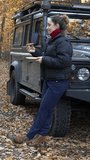 Female is eating meal next to a parked 4x4 car. Overland travel adventure. Vertical video.