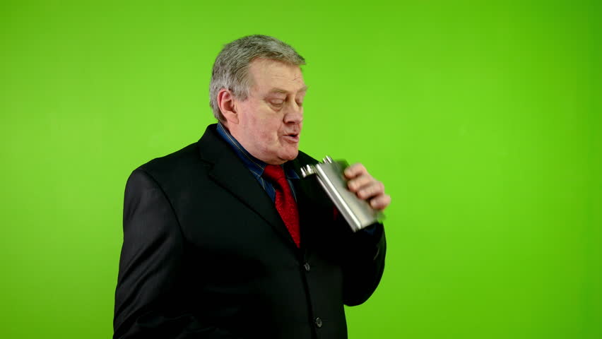 Senior businessman in black suit drinks alcohol from flask while working. Mature person with alcoholism addiction, quietly drinks violating rules. Green Screen. Chroma key.