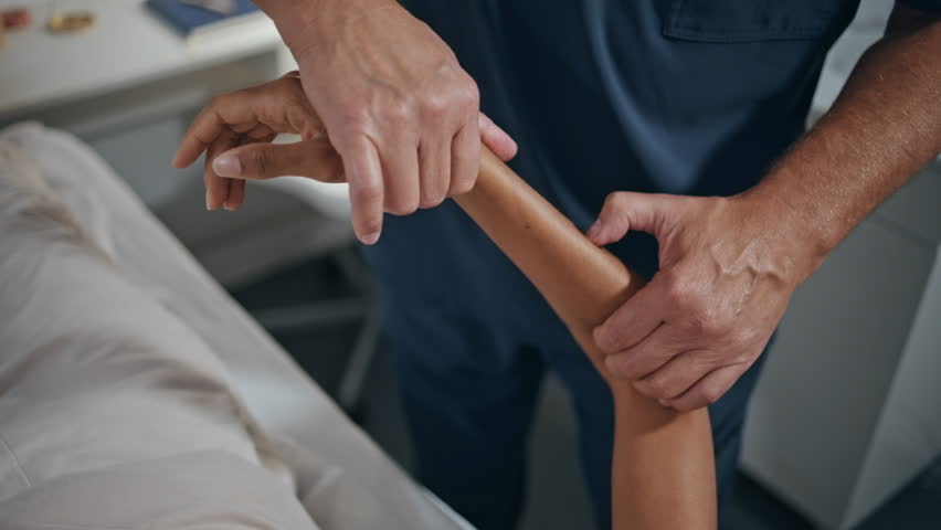 Closeup osteopath treating hand on therapy session. Physiotherapist examine arm doing recovery exercise in rehabilitation clinic. Unknown man chiropractor healing work with patient in medical center