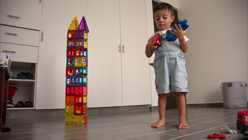 Slow motion of a young latin boy next to a tower made of magnetic tiles with toy cars in it smiling and lifting his eyebrows Royalty-Free Stock Footage #3444779655