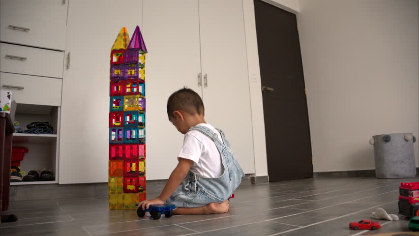 Slow motion of a naughty young latin hispanic toddler destroying a tower made of magnetic tiles with toy cars inside it Royalty-Free Stock Footage #3444779921
