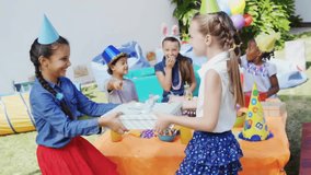 Animation of confetti over happy diverse girls playing with present at birthday party. Childhood, fun, party, birthday and celebration, digitally generated video.