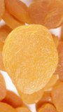 Vertical video. Top view, dried apricot rotates against the background of a heap of other dried apricots.