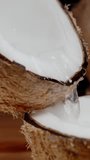 Vertical video. Two halves of a broken coconut, and juice flows from one half to the other, in slow motion.