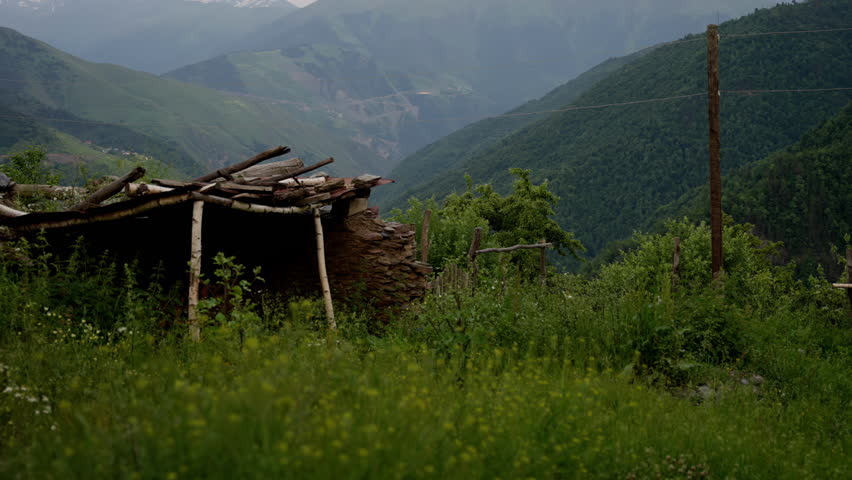Old stone shelter remains in lush mountain greenery.Rustic stone shelter with a collapsed wooden roof in a verdant mountain valley