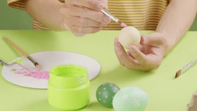 Front view of a young man decorating eggs to give to relatives on Easter. On a green background, colorful eggs, paintbrush and color jar decorated.