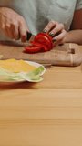 Vertical video. Home Life and Food Preparation, a woman slices tomatoes into slices, and the camera zooms in closer. Homemade burgers.