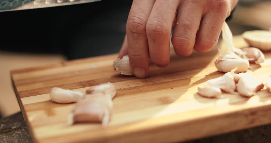A man peels fresh garlic with his hands. Preparation for cooking. Outdoor cooking.