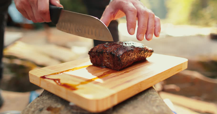 A man is slicing a juicy, freshly cooked steak outdoors.