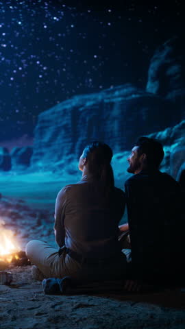 Vertical Video: Happy Couple Camping in the Canyon, Sitting by Campfire Watching Night Sky with Milky Way Ful of Bright Stars. Two Nature Travelers In Love On a Romantic Vacation Trip. Back View