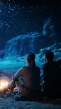 Vertical Video: Happy Couple Camping in the Canyon, Sitting by Campfire Watching Night Sky with Milky Way Ful of Bright Stars. Two Nature Travelers In Love On a Romantic Vacation Trip. Back View