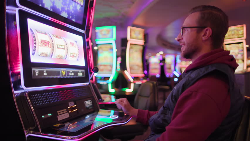 An ecstatic young male pumps his fist in victory at a brightly lit slot machine in a casino, signaling a big win, Jackpot. Slow Motion, 4K RAW.  Royalty-Free Stock Footage #3444915227