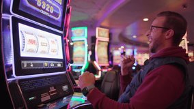 An ecstatic young male pumps his fist in victory at a brightly lit slot machine in a casino, signaling a big win, Jackpot. Slow Motion, 4K RAW.  - Powered by Shutterstock - Get 15% off with code: PIKWIZARD15