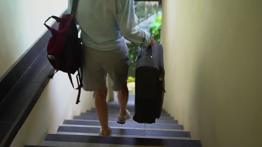 An elderly woman comes down the stairs with a suitcase, pensioner going on a trip with luggage bags in hands.