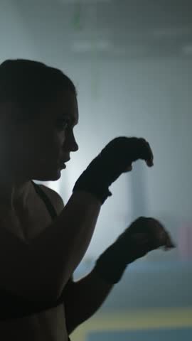 Woman fighter trains his punches and defense in the boxing gym, the girl strikes fast, vertical video.
