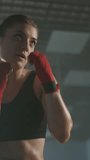 Caucasian woman fighter trains his punches and defense in the boxing gym, the girl strikes fast, slow motion vertical video.