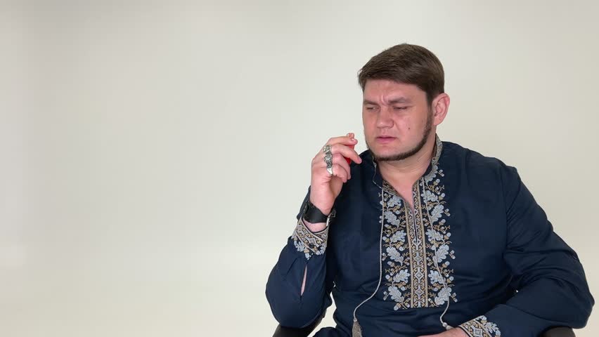 exhaling smoke Ukarinsky Cossack smokes pipe he looks serious thoughtfully dressed in a blue vyshyvanka with white embroidery neat beard thick hair Ukrainian  Royalty-Free Stock Footage #3445005619