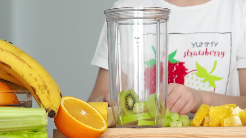 girl prepares fresh organic smoothie from fruits. Healthy eating concept: close-up of mixing apples, kiwi, orange and bananas in a blender to make a smoothie.