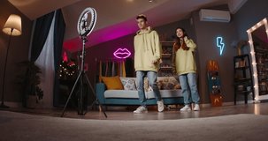Guy and girl are filming new video for social networks, synchronized dance movements are filmed by smartphone mounted on ring lamp on tripod. Young people record dance videos for their channel. AD.