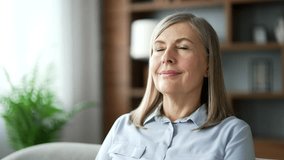 Senior female relaxing with her eyes closed while sitting in the living room. Portrait of a calm happy elderly woman resting breathing deeply on comfortable couch at home. Meditation concept. Close up - Powered by Shutterstock - Get 15% off with code: PIKWIZARD15