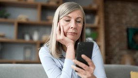 Lonely sad senior gray haired female bored using smartphone sitting on sofa in living room at home. Tired elderly retired woman is depressed and in a bad mood, browses social media on a mobile phone - Powered by Shutterstock - Get 15% off with code: PIKWIZARD15