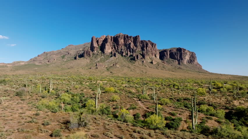 Saguaro cactus and yellow shrubs line thin sandy hiking trail leading to base of Superstition Mountains Arizona Royalty-Free Stock Footage #3445105331