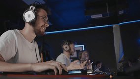 Bristly adult gamer in headset playing PC video game at computer club with team cyber sport tournament. E-sport championship. 5 player in headphones. Multiplayer online real-time strategy shooter