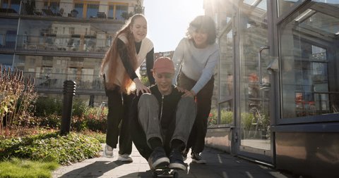 Teenager girls pushing friend sitting on skateboard near apartment blocks 库存视频