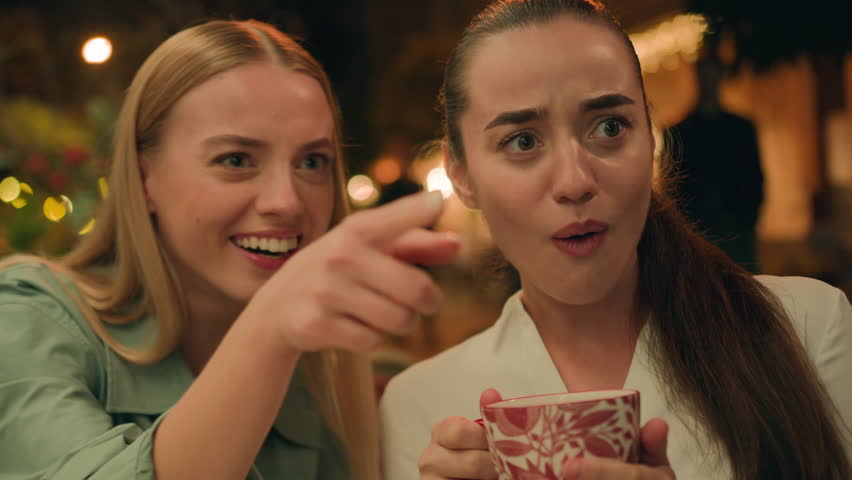 Two Caucasian European women friends talking city cafe outside pointing finger sisters friendship gesture surprised amazed shocked discuss gossiping expression chatting girlfriend secret curious laugh