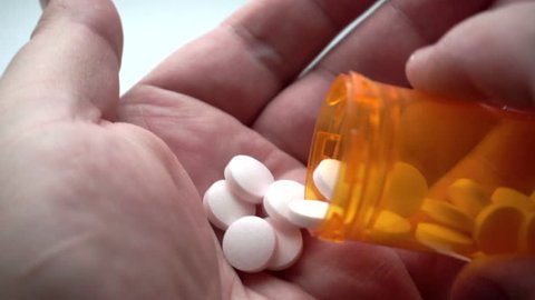 Man takes and shows pills vitamins or drugs tablets in hand from pill bottle, macro shot 