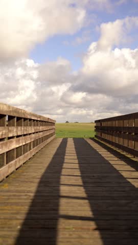 A cloudy day in the Swedish countryside. Wooden path running towards the fields. Sun is shining through the clouds, relaxed mood. Skåne, Malmö. Vertical