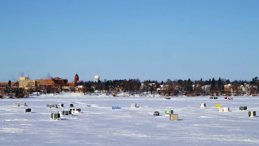 Pickup Truck Drives on Frozen Lake with Winter Fish Houses in Foreground and Bemidji Minnesota in Background on a Sunny Day