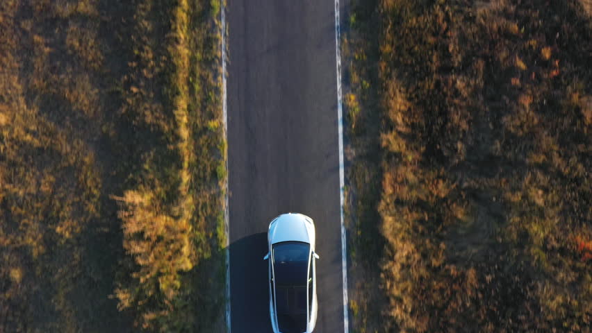 Aerial shot of electrical car driving on country road at summer evening. New SUV vehicle speeding through highway. Ecology friendly car riding on electric charge along motorway. Top view Close up